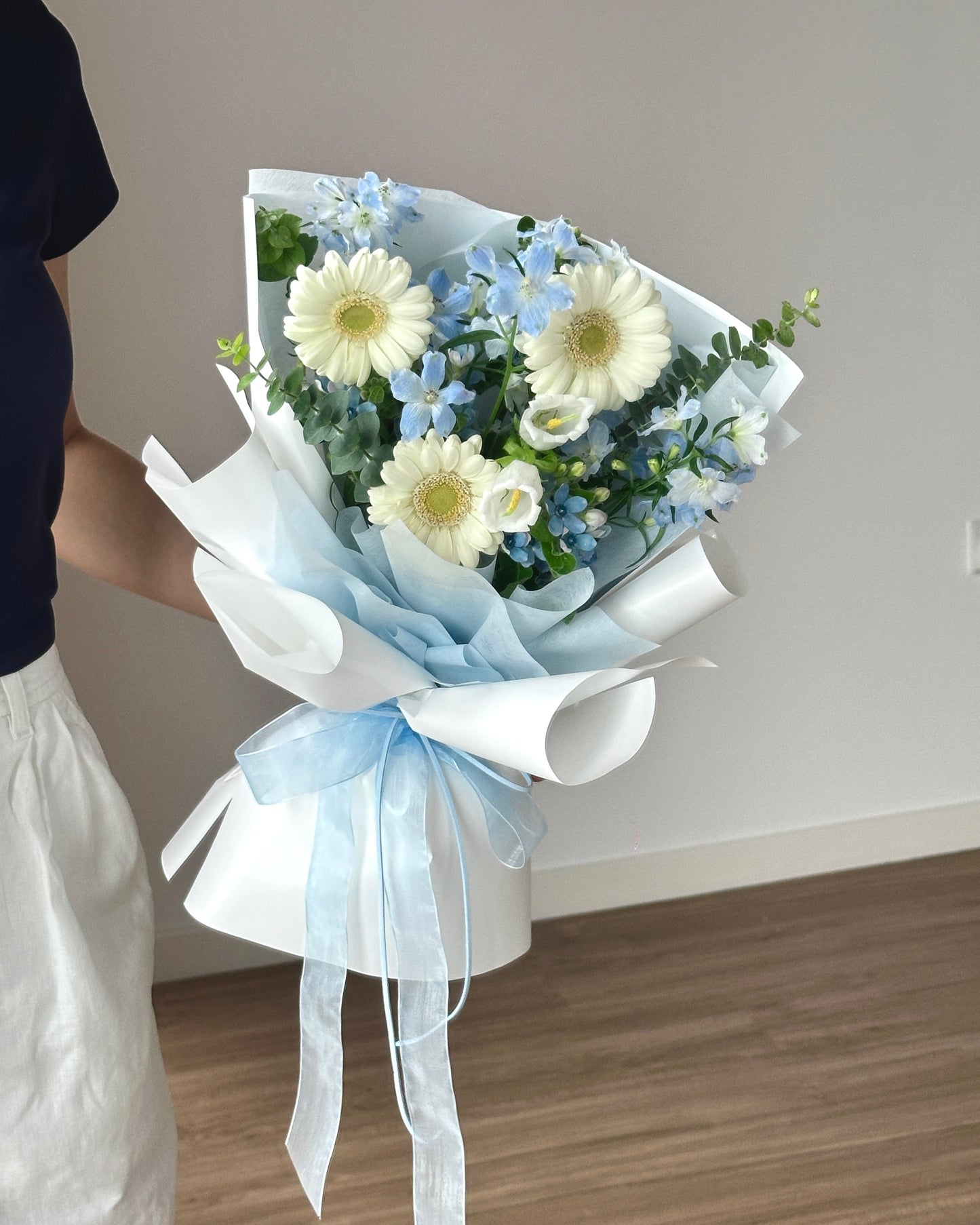 Bouquet of flowers with a white and light blue ribbon held by a person.