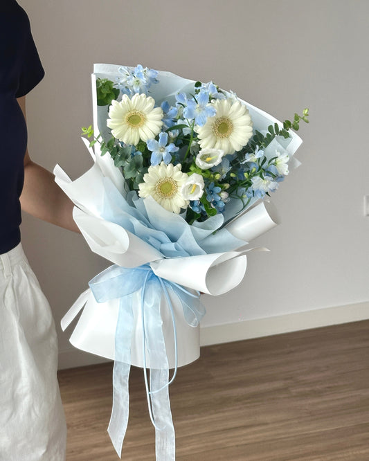Bouquet of flowers with a white and light blue ribbon held by a person.